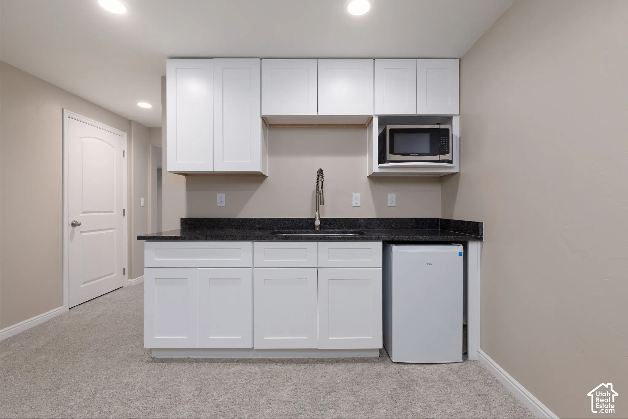 Built-in kitchenette featuring white cabinetry, dark countertop, undermount sink, and stainless steel microwave