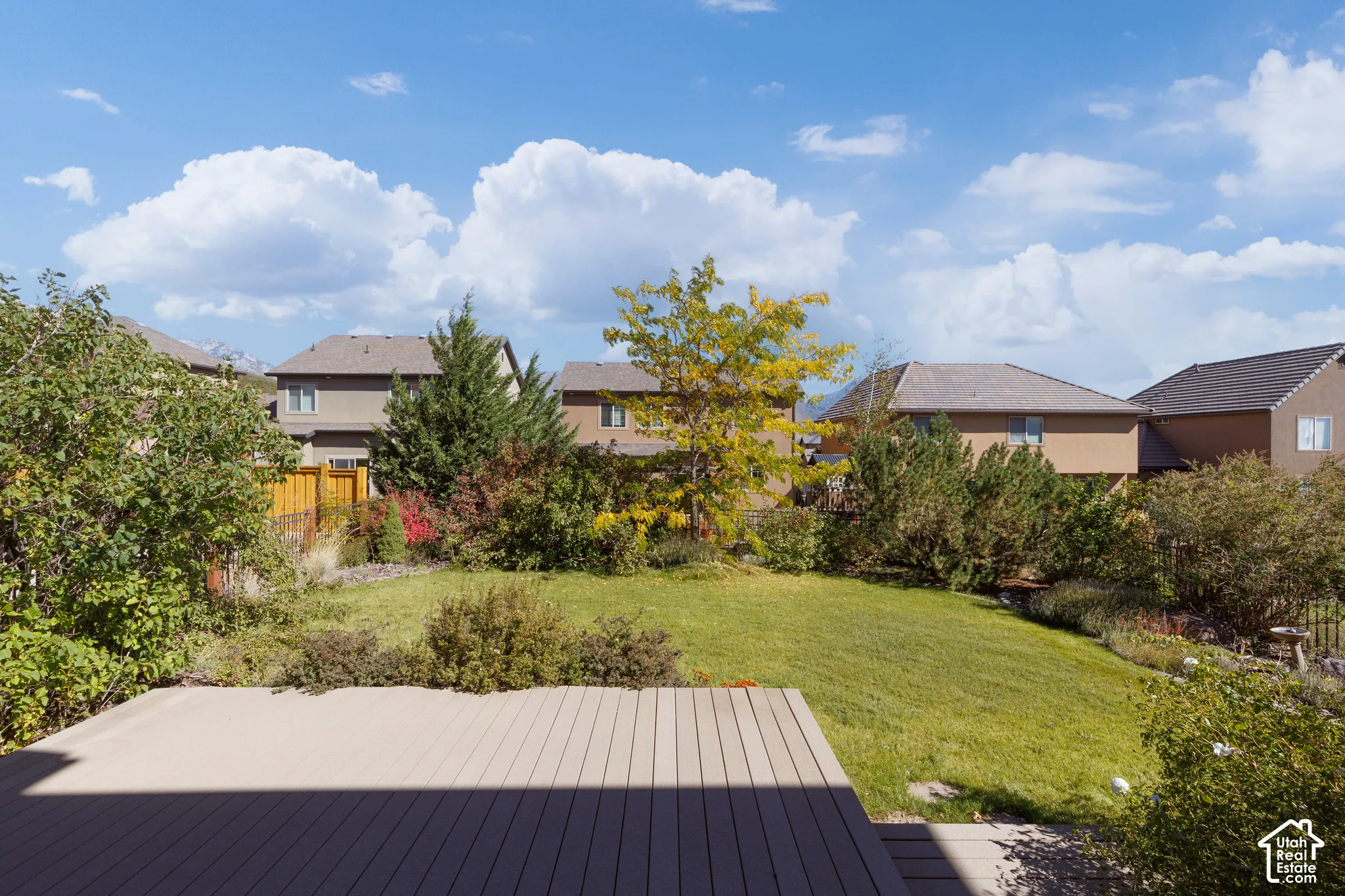 Expansive backyard featuring a manicured lawn, established landscaping, and a composite deck