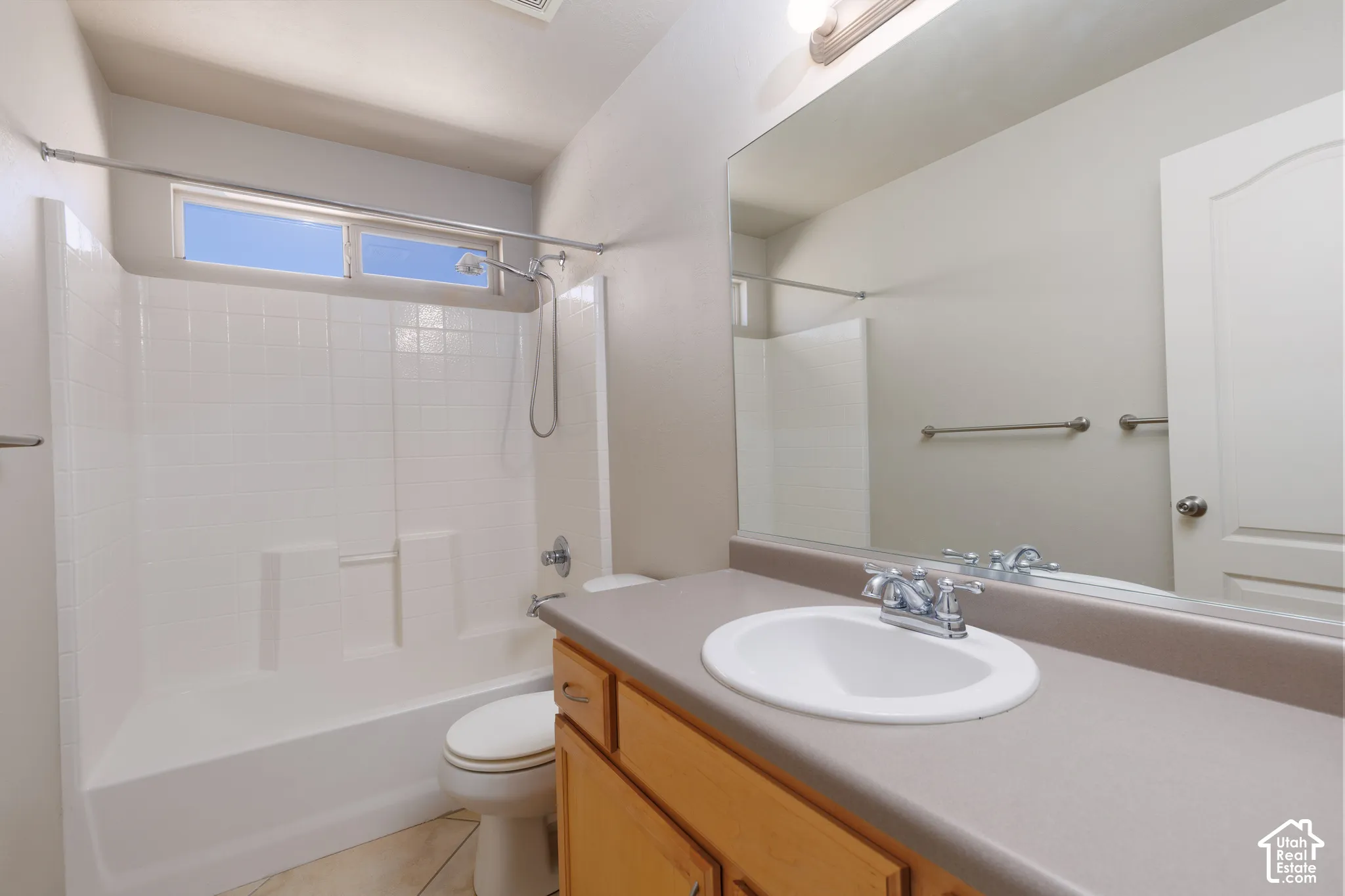 Full bath featuring a tub/shower combination with white tile surround, wood-finish vanity with an integrated sink, and an expansive wall-mounted mirror