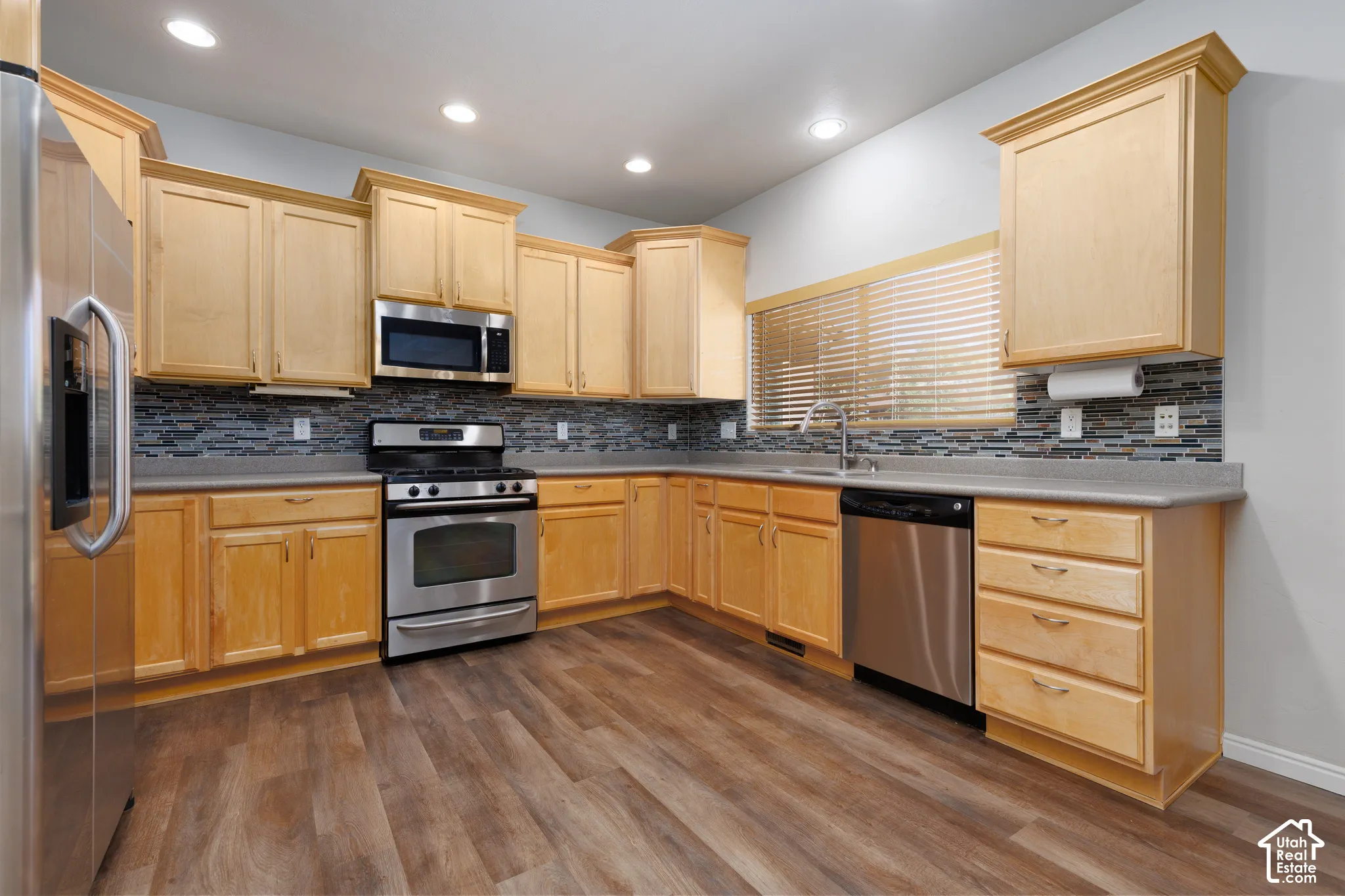 Wood-finish flooring, light wood cabinetry, stainless steel appliances, and a tiled backsplash