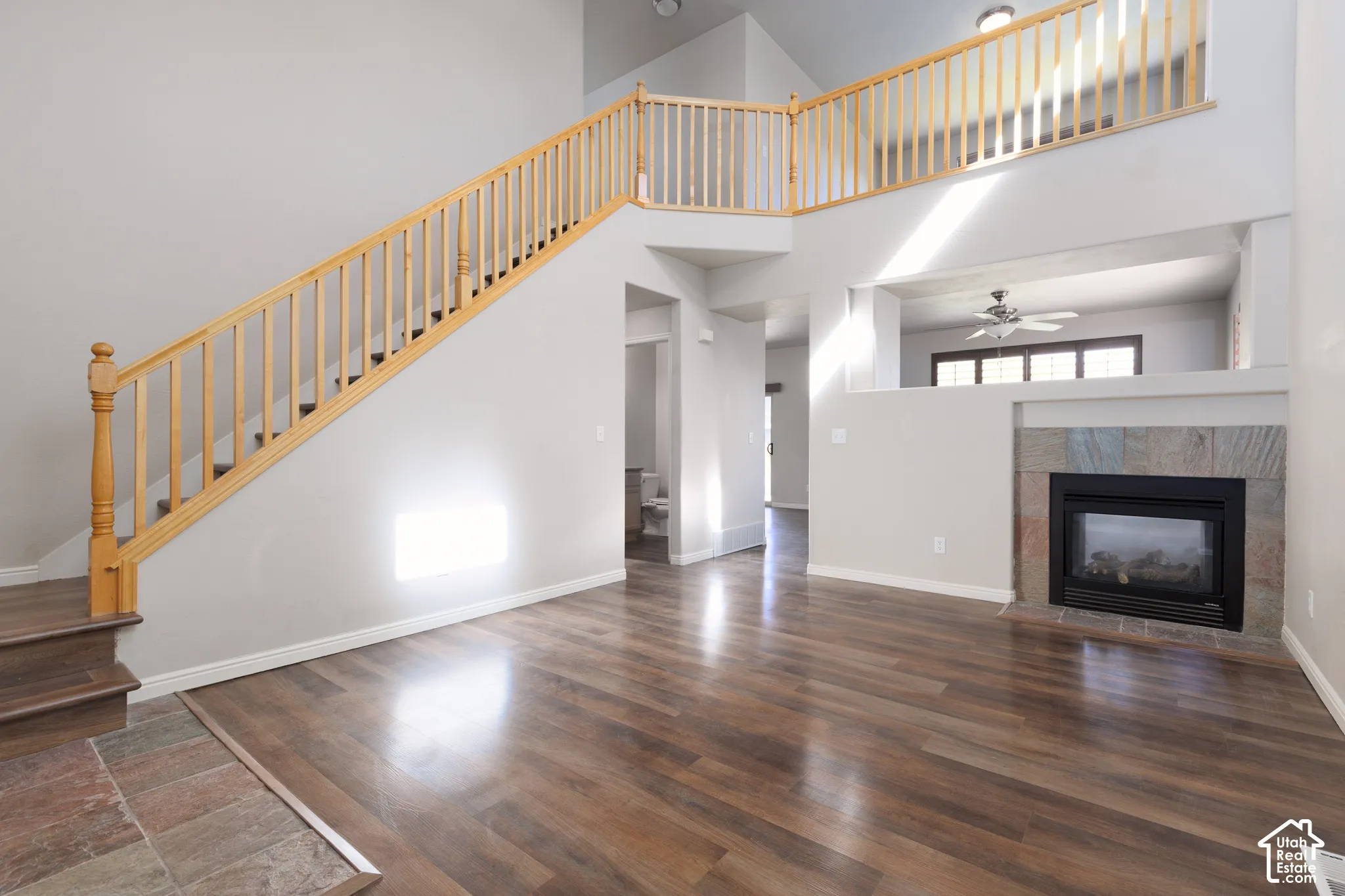 Vaulted ceiling, wood-finish flooring, staircase with natural wood railing, stone-clad fireplace, and an open-concept upper-level walkway