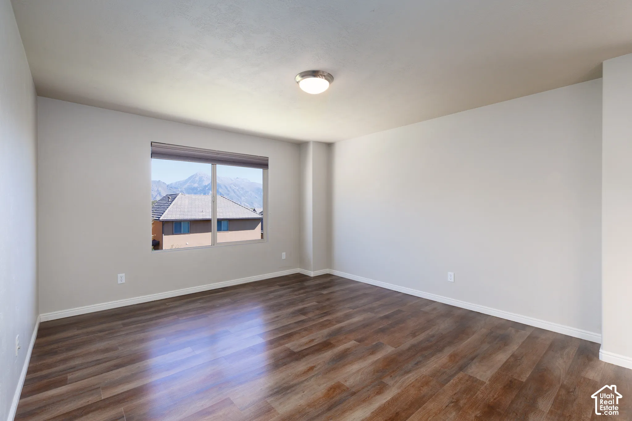 Spacious room with wood-finish flooring, neutral wall paint, and a window featuring mountain scenery