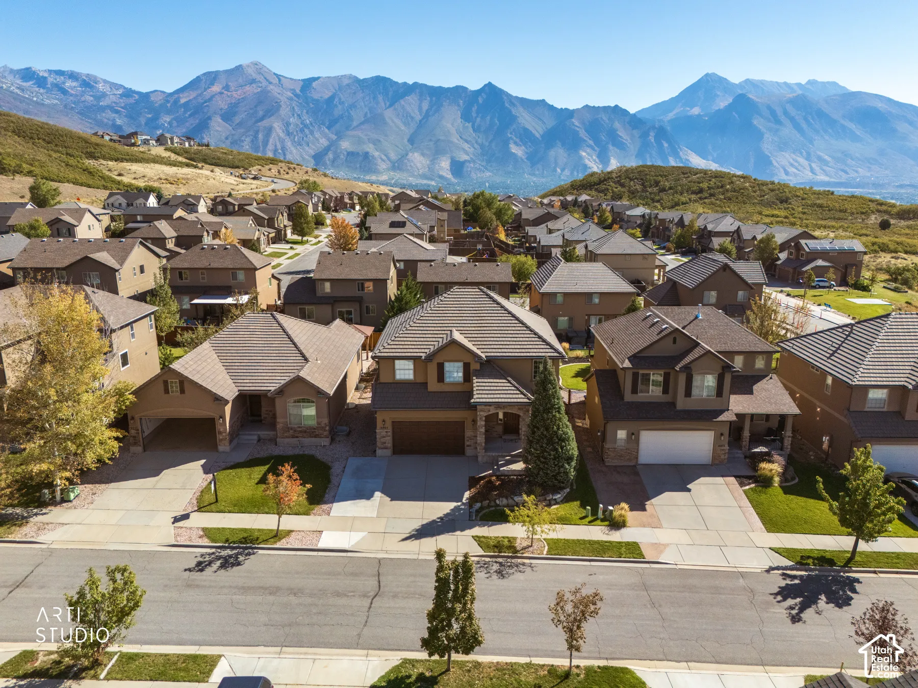 Mountain-backed neighborhood setting featuring multiple residential properties with pitched roofs, varied exterior finishes, and attached garages