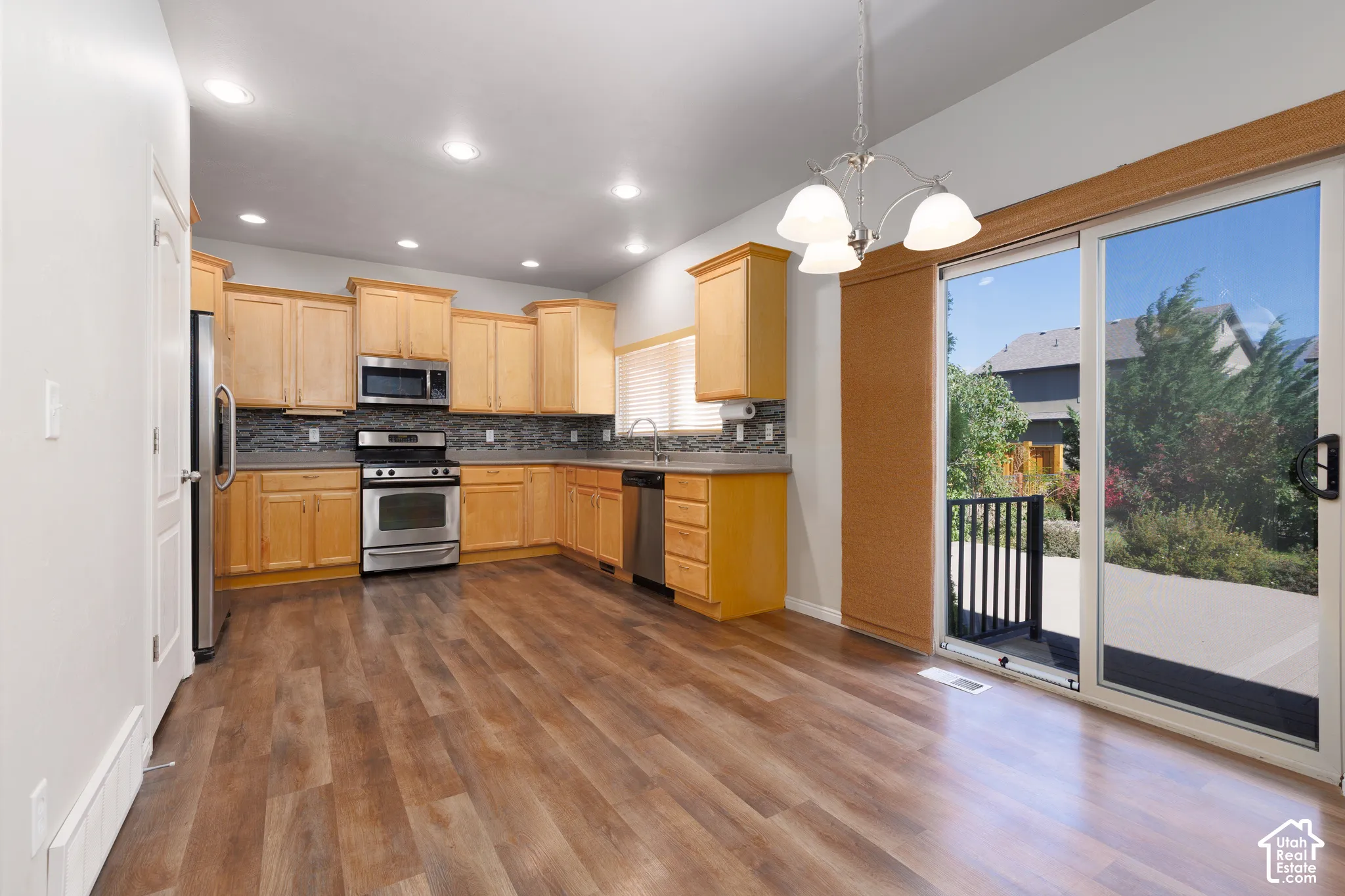 Kitchen featuring wood-finish flooring, stainless steel appliances, light wood cabinetry, and a sliding glass door