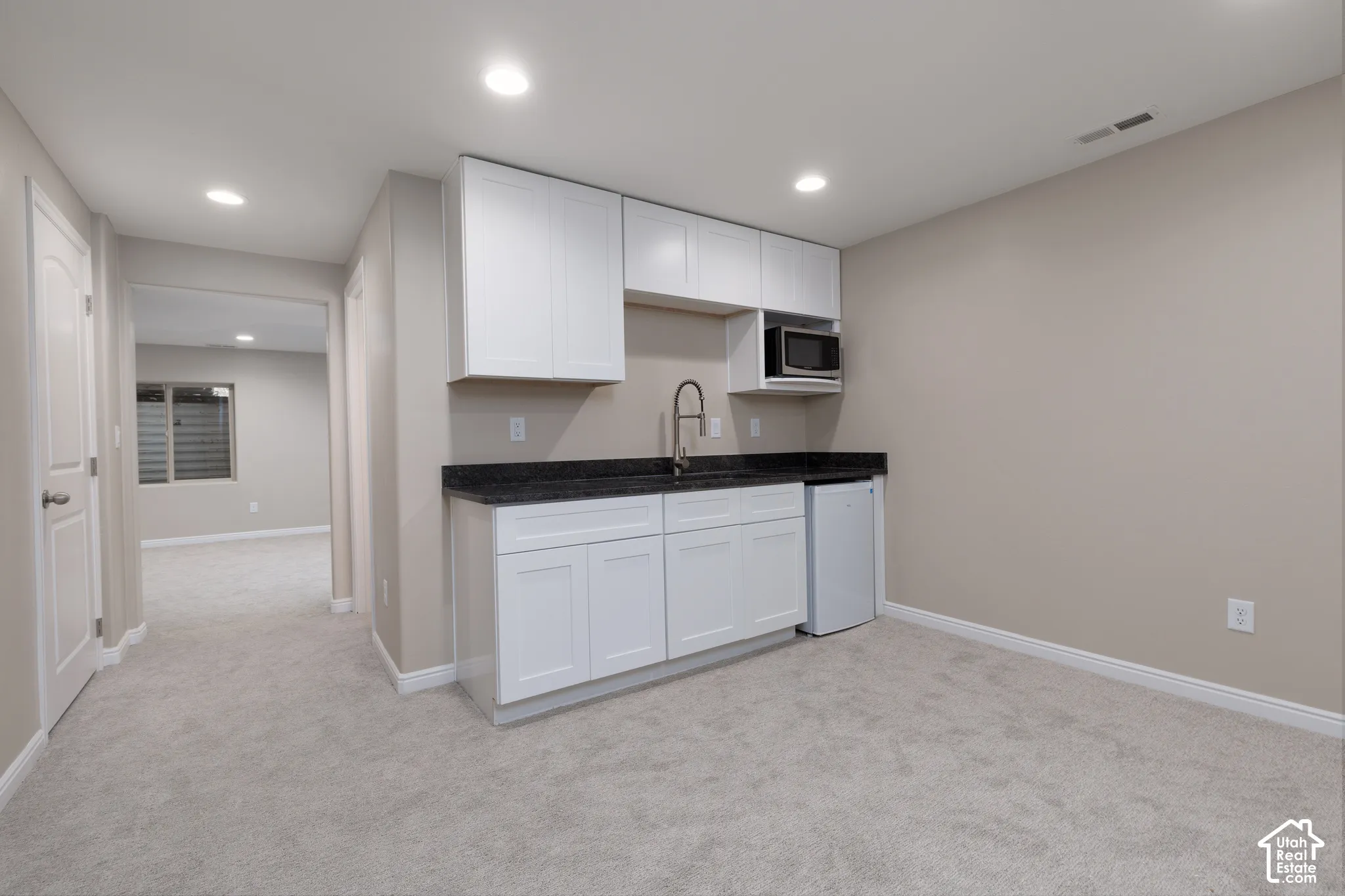 Built-in wet bar with white cabinetry, dark stone countertop, and stainless steel sink