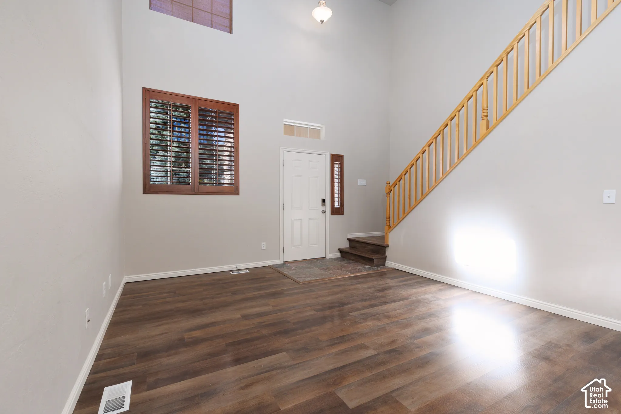 Wood-finish flooring with a light gray wall color, a white entry door, and a staircase with natural wood balusters