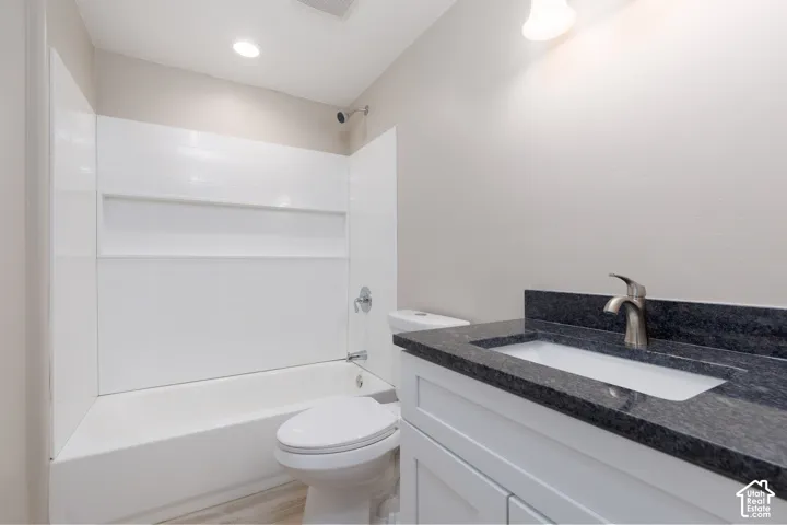 White bathtub with an integrated shower, white toilet, white vanity with a dark countertop, and a brushed nickel faucet