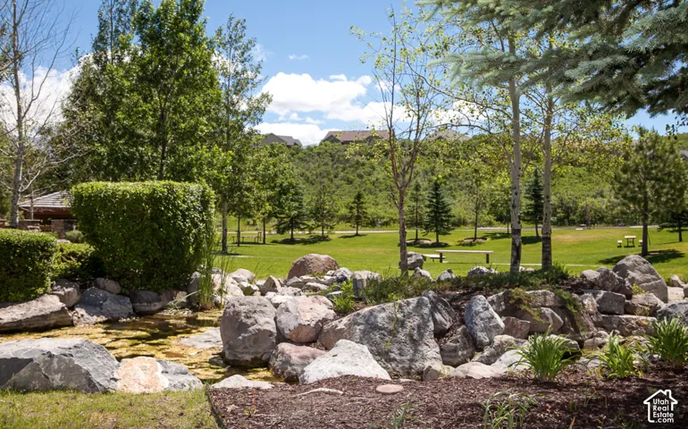 Rock feature with established plantings, bordering a water element, surrounded by a manicured lawn and mature trees