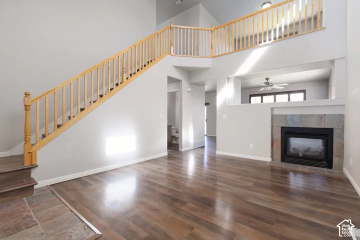 Vaulted ceiling, wood-finish flooring, staircase with natural wood railing, stone-clad fireplace, and an open-concept upper-level walkway