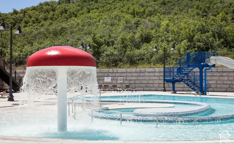 Outdoor pool area featuring a water mushroom, water slide structure, and a retaining wall