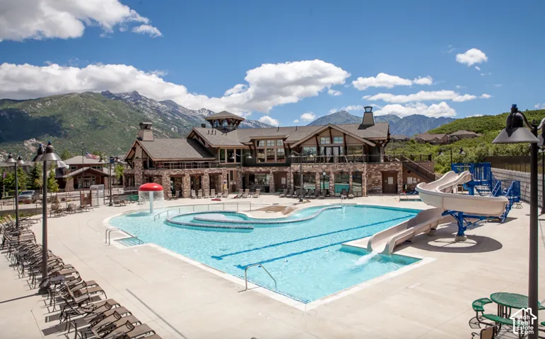 Expansive outdoor pool with integrated slides and a separate water feature, surrounded by a large concrete deck with abundant lounge seating