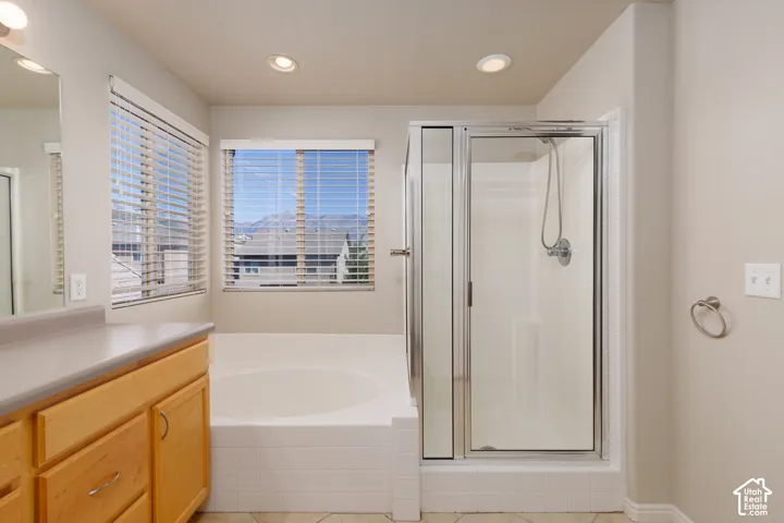 Recessed lighting, wood-finish cabinetry, built-in bathtub, glass-enclosed shower, and tile flooring