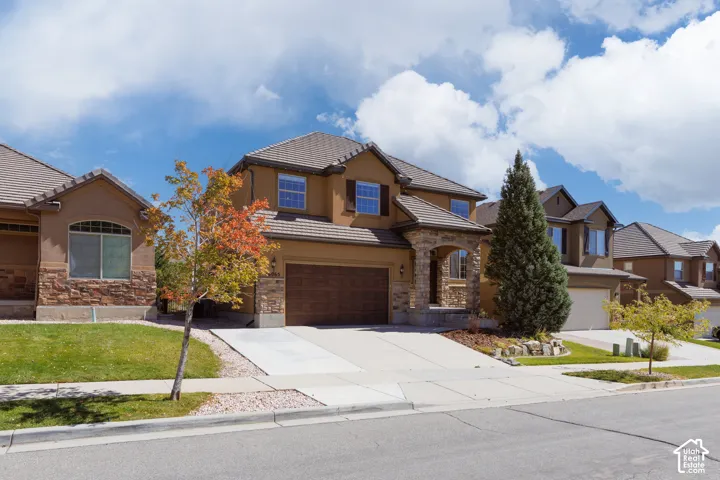 Two-story stucco and stone exterior with an attached two-car garage, concrete driveway, and mature landscaping