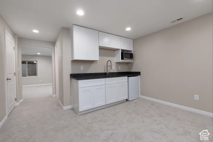 Built-in wet bar with white cabinetry, dark stone countertop, and stainless steel sink