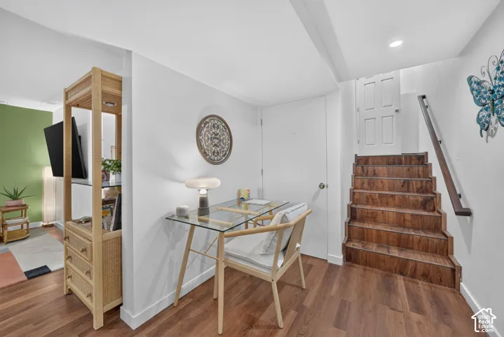 Wood-finish flooring, white walls, wood staircase with dark railing, white paneled door