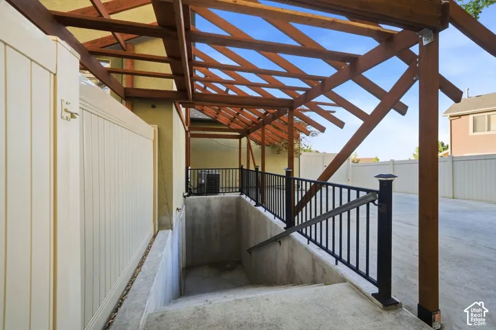 Pergola-covered entry with exposed wood beams, concrete stairs, and black metal railings