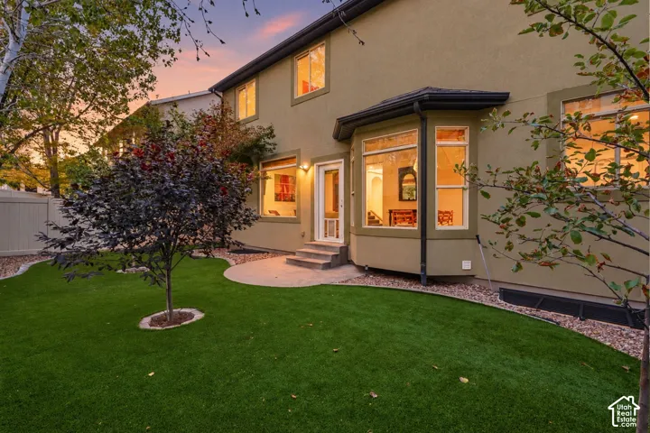 Expansive backyard featuring artificial turf, mature trees, a concrete patio, and a stucco exterior with multiple windows