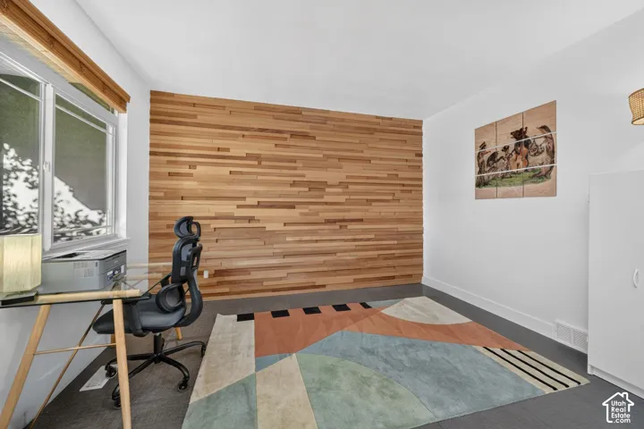 Wood-paneled accent wall, white painted walls, window with wood blinds, built-in white cabinetry, and gray flooring