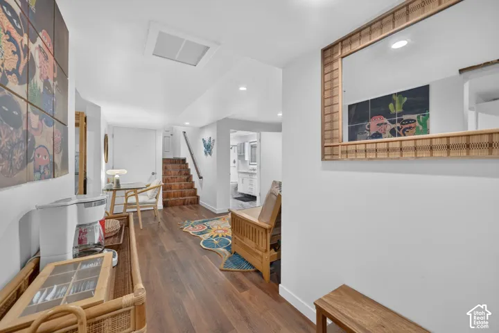 Wood-finish flooring throughout, white walls, recessed ceiling lighting, and a staircase with wood treads and a dark handrail