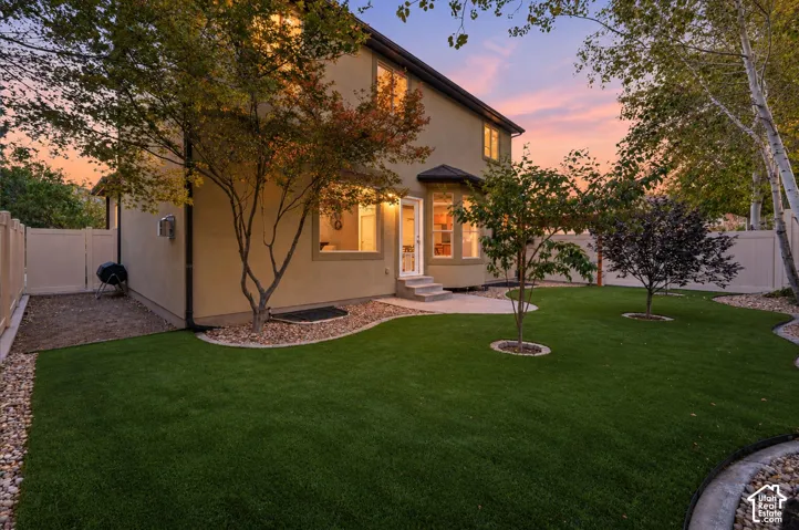 Manicured lawn with a concrete patio, mature trees, and decorative rock landscaping