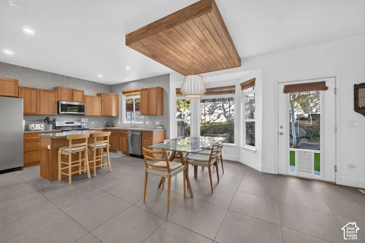 Kitchen and dining area featuring light wood cabinetry, stainless steel appliances, a center island with seating, a bay window, and a wood-finish ceiling accent