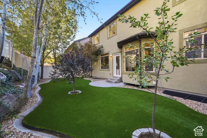 Expansive rear yard featuring a manicured lawn, established trees, a paver patio, and stone landscaping