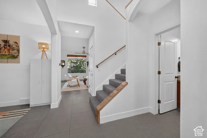 Foyer featuring large format floor tiles, carpeted staircase with wood handrail, and high ceilings