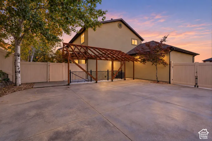 Expansive concrete driveway with a custom wood pergola, black metal railing, and a privacy fence