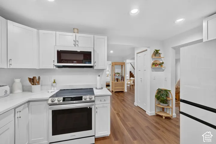 White cabinetry with brushed nickel hardware, built-in microwave, wood-finish flooring, recessed lighting, and a stainless steel range