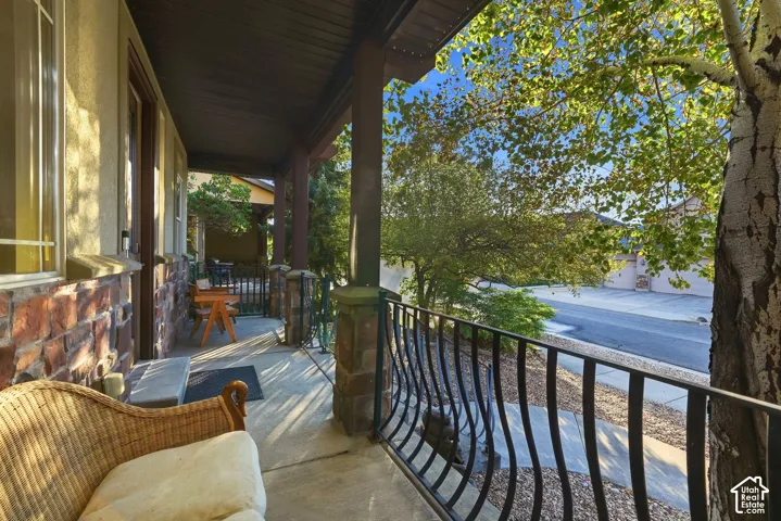 Covered concrete porch with stone-clad columns, stucco siding, and a decorative wrought iron railing