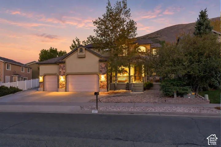 Stucco exterior with stone accents, covered front porch, dual garage doors, and a terraced front yard
