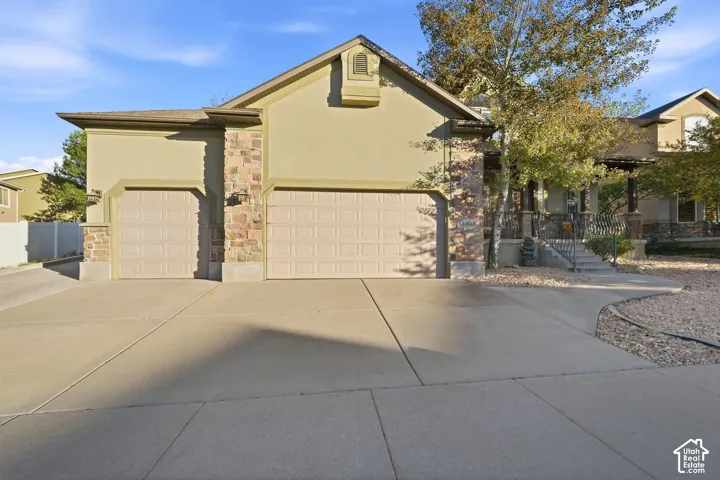 Stucco exterior with stone accents, featuring a two-car garage, an additional single-car garage, and a concrete driveway