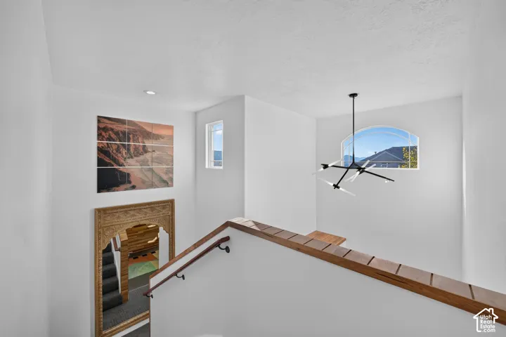 Arched window, modern chandelier, recessed lighting, wood-finish railing, white walls