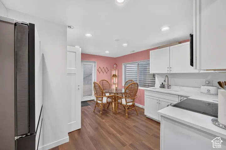 Wood-finish flooring, recessed lighting, white cabinetry, integrated cooktop, and a stainless steel sink with a gooseneck faucet