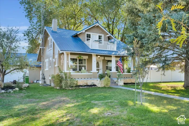 Craftsman-style exterior featuring a standing-seam metal roof, a stone-base front porch with square columns, and a second-story balcony with white railing
