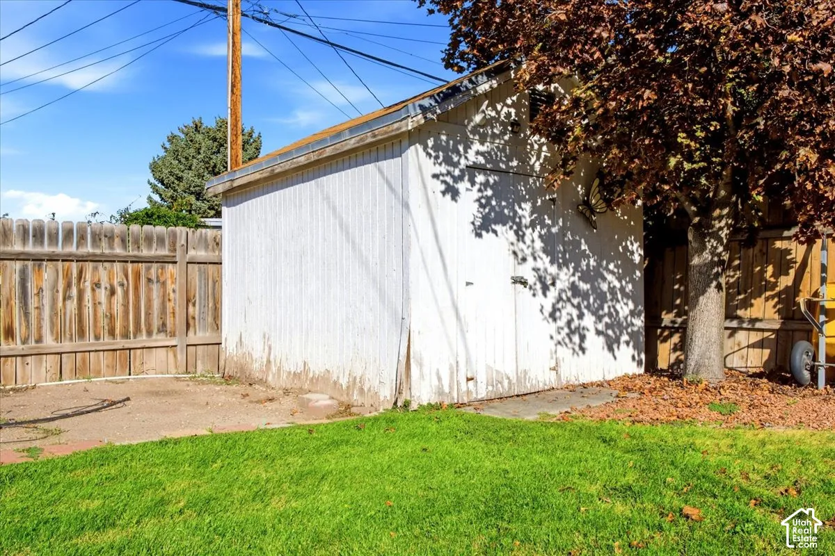 Wooden privacy fence, mature tree, grass lawn, concrete pad, white utility building