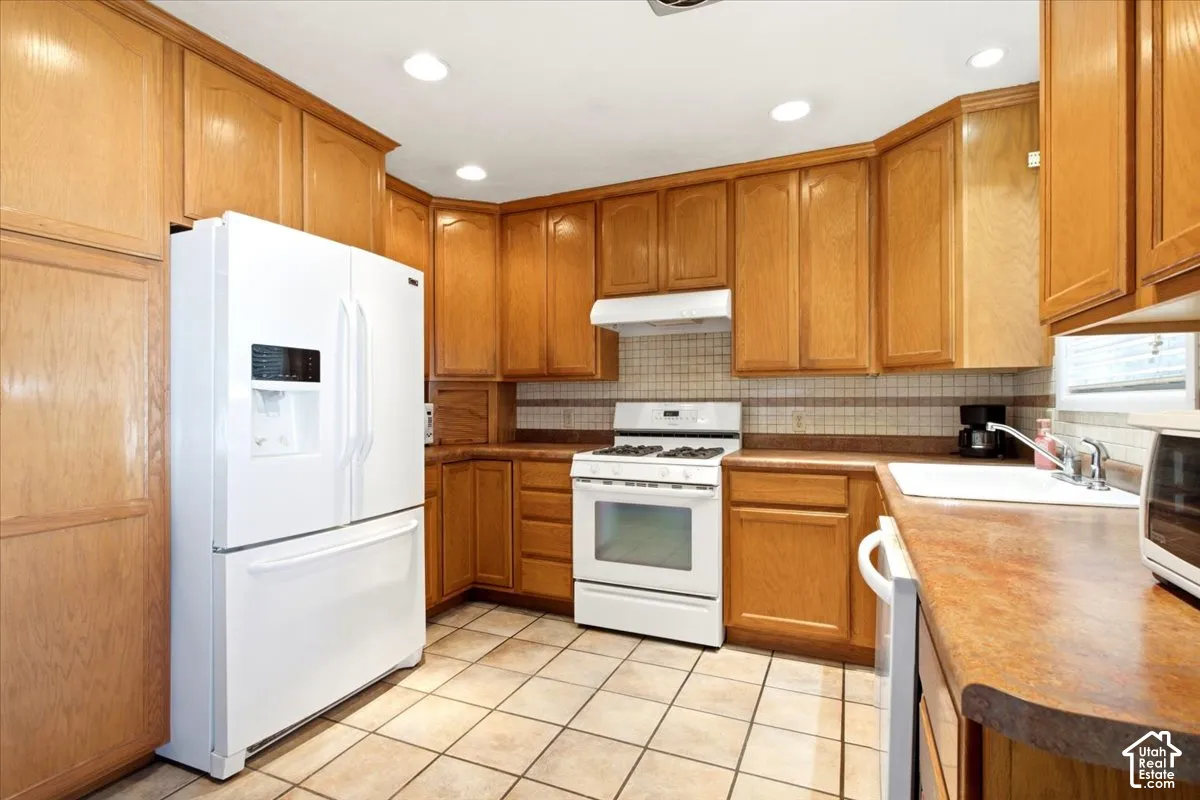 Kitchen featuring wood-finish cabinetry, white appliances, recessed lighting, and tile flooring