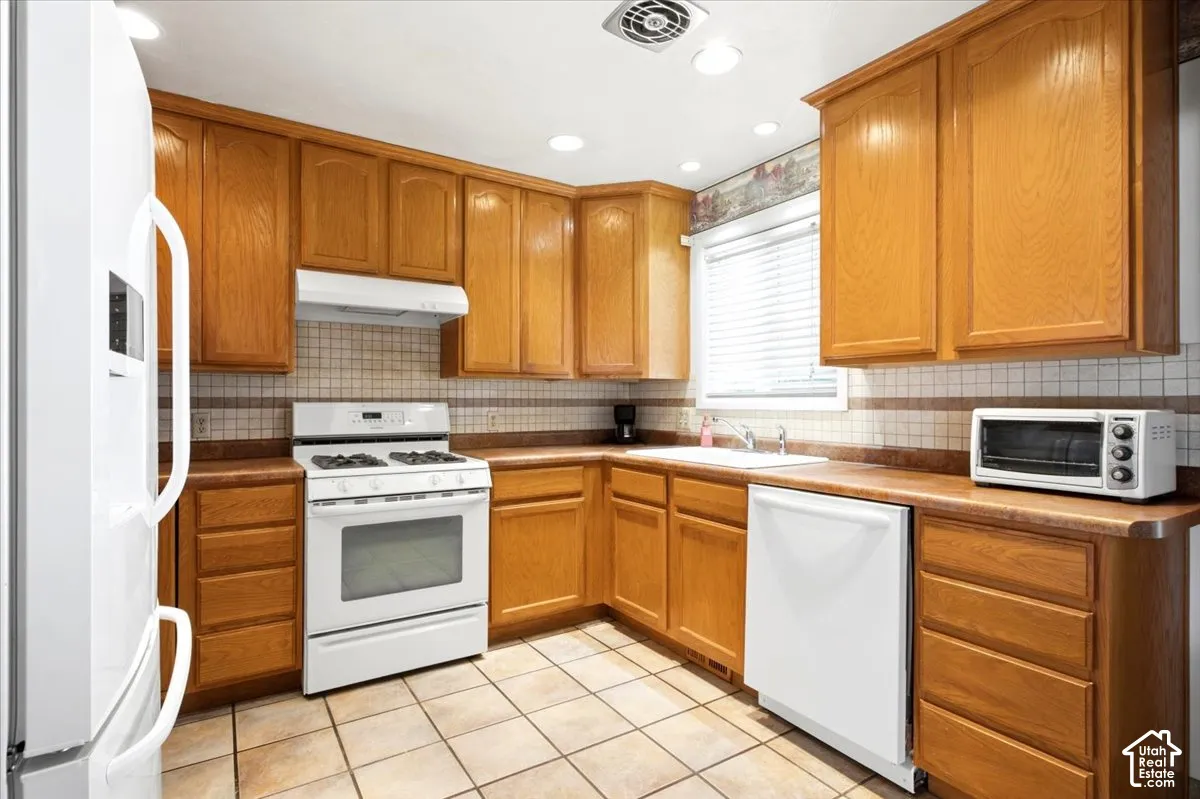 Kitchen featuring wood cabinetry, a white gas range, a white dishwasher, a white refrigerator, and tile flooring