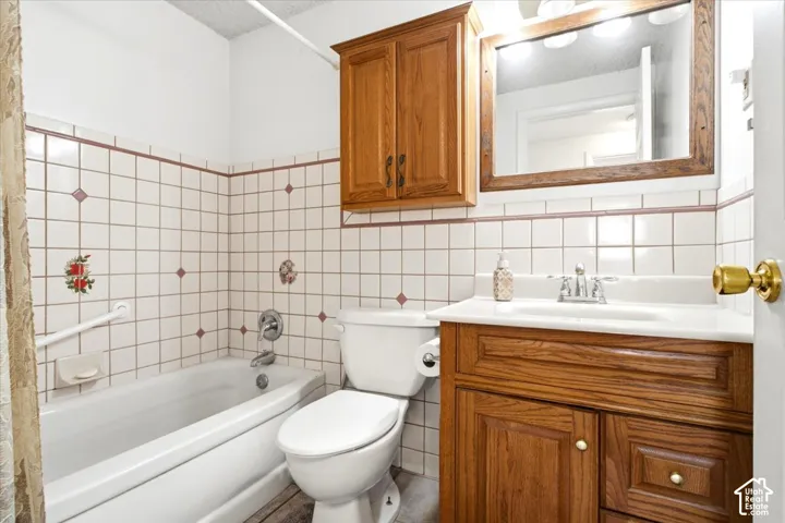 Bathroom featuring a built-in tub, white tile surround with decorative accents, wood-finish vanity with a white countertop, and a wood-frame mirror