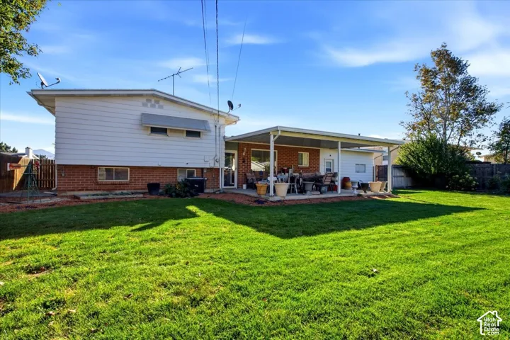 Expansive green lawn, covered patio, brick and siding exterior, mature landscaping, and privacy fencing
