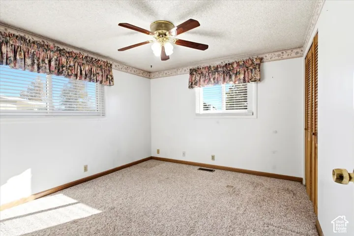 Carpeted room featuring a ceiling fan with light fixture, two windows with blinds, and a built-in closet with louvered doors