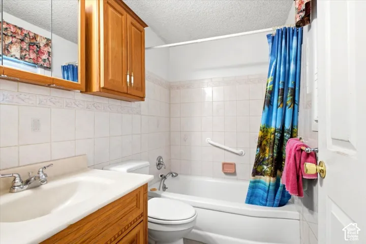 Bathroom featuring a single vanity, a built-in bathtub, a toilet, and ceramic tile walls