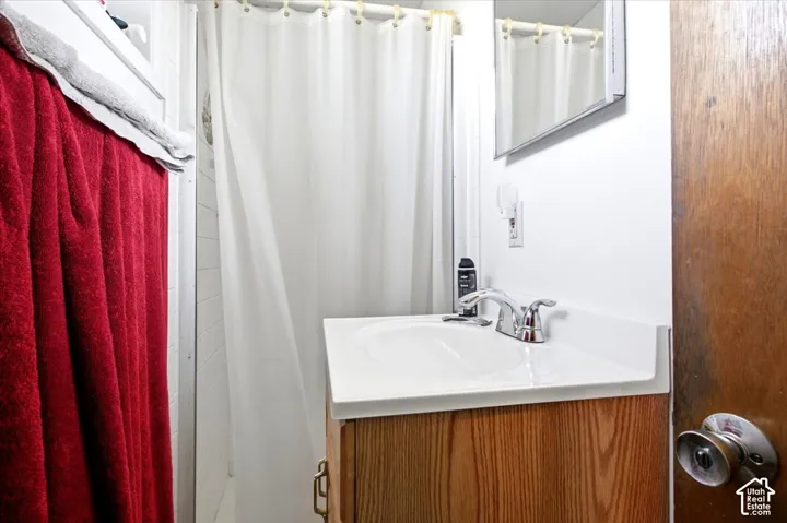 Bathroom vanity with light wood-finish cabinetry, integrated white countertop and sink, and chrome faucet