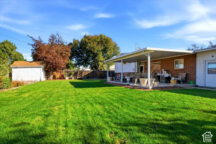 Expansive green lawn, covered patio, brick exterior, dedicated storage shed, and mature trees
