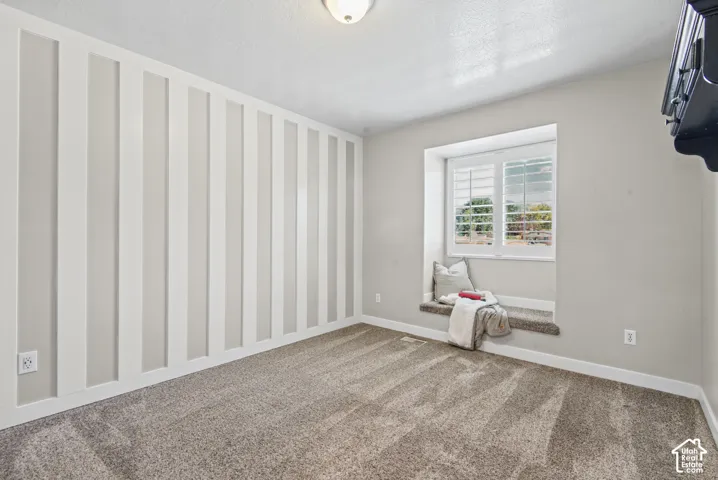 Textured accent wall, window with plantation shutters, integrated window seat, and carpet flooring
