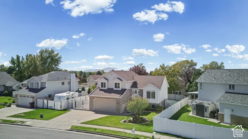 White siding exterior with brick accents, attached two-car garage, manicured lawn, and mature trees