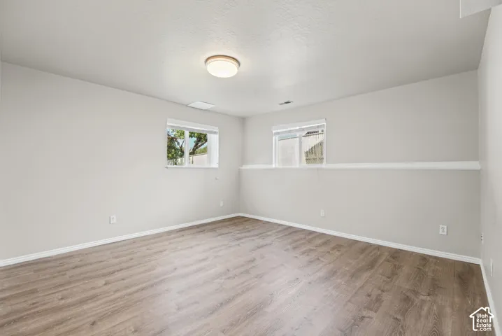 Daylight basement windows, wood-finish flooring, neutral wall tones, and overhead lighting
