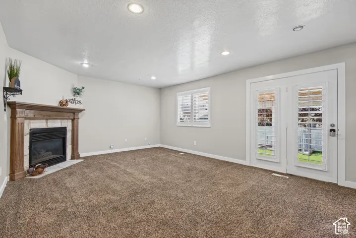 Fireplace with stone surround and wood mantle, white plantation shutters, dual French doors with glass panels, recessed lighting, and carpet flooring