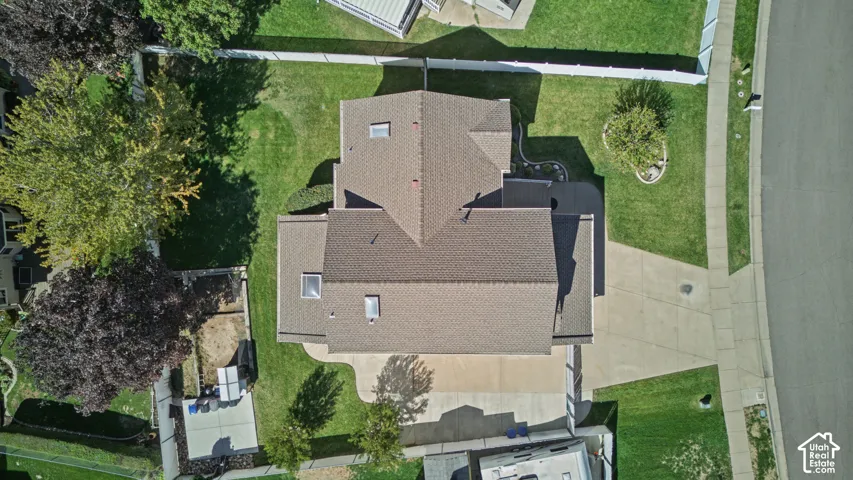 Asphalt shingle roofing, skylights, concrete driveway, manicured lawn, and mature trees