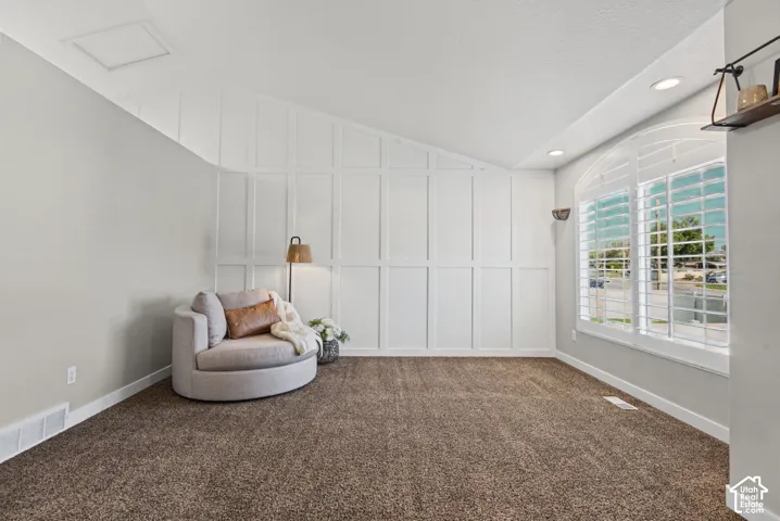 Vaulted ceiling, accent wall with paneling, recessed lighting, arched window with plantation shutters, and carpet flooring